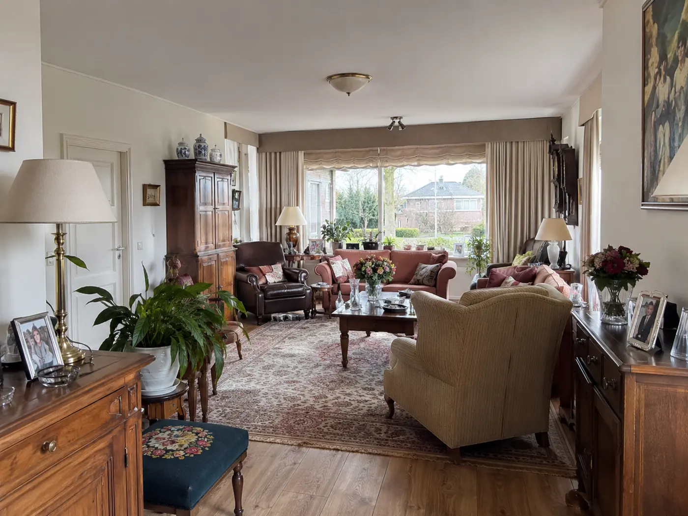 Woonkamer vóór de ontruiming, met klassieke meubels, vloerkleed, fauteuils en persoonlijke decoratie.