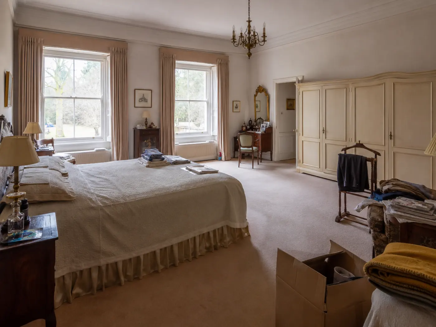 Grote slaapkamer vóór de ontruiming, met bed, kasten, kleding, dozen en overige inboedel.
